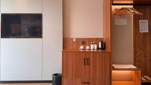Una habitación pequeña con un armario de madera, una mesita con tazas y una tetera, y un guardarropa de madera con espejo.