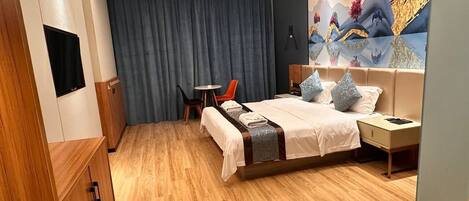 Une chambre d’hôtel moderne avec un plancher en bois, un lit recouvert d’une courtepointe blanche et marron, une petite table avec une chaise, une table de chevet et une grande fresque murale.