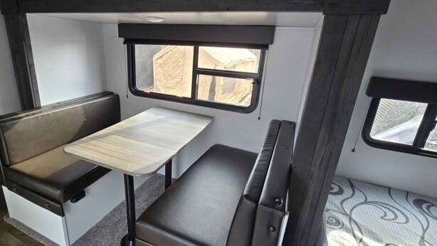 A compact RV interior with a small table, bench seating, and a window providing a view outside.