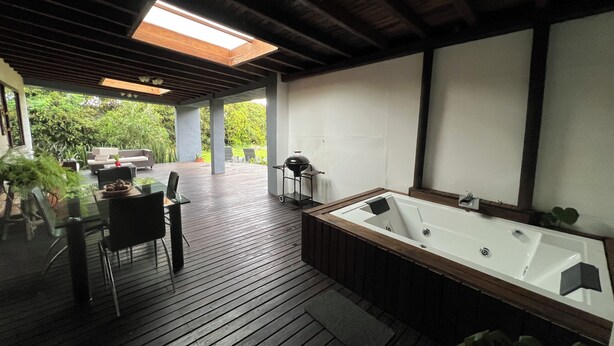 A wooden deck with a hot tub, outdoor seating, and a view of greenery. - Beautiful country (Rionegro)
