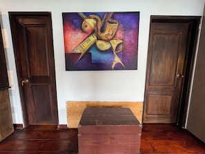 A room with a wooden floor, a painting on the wall, and two closed doors.