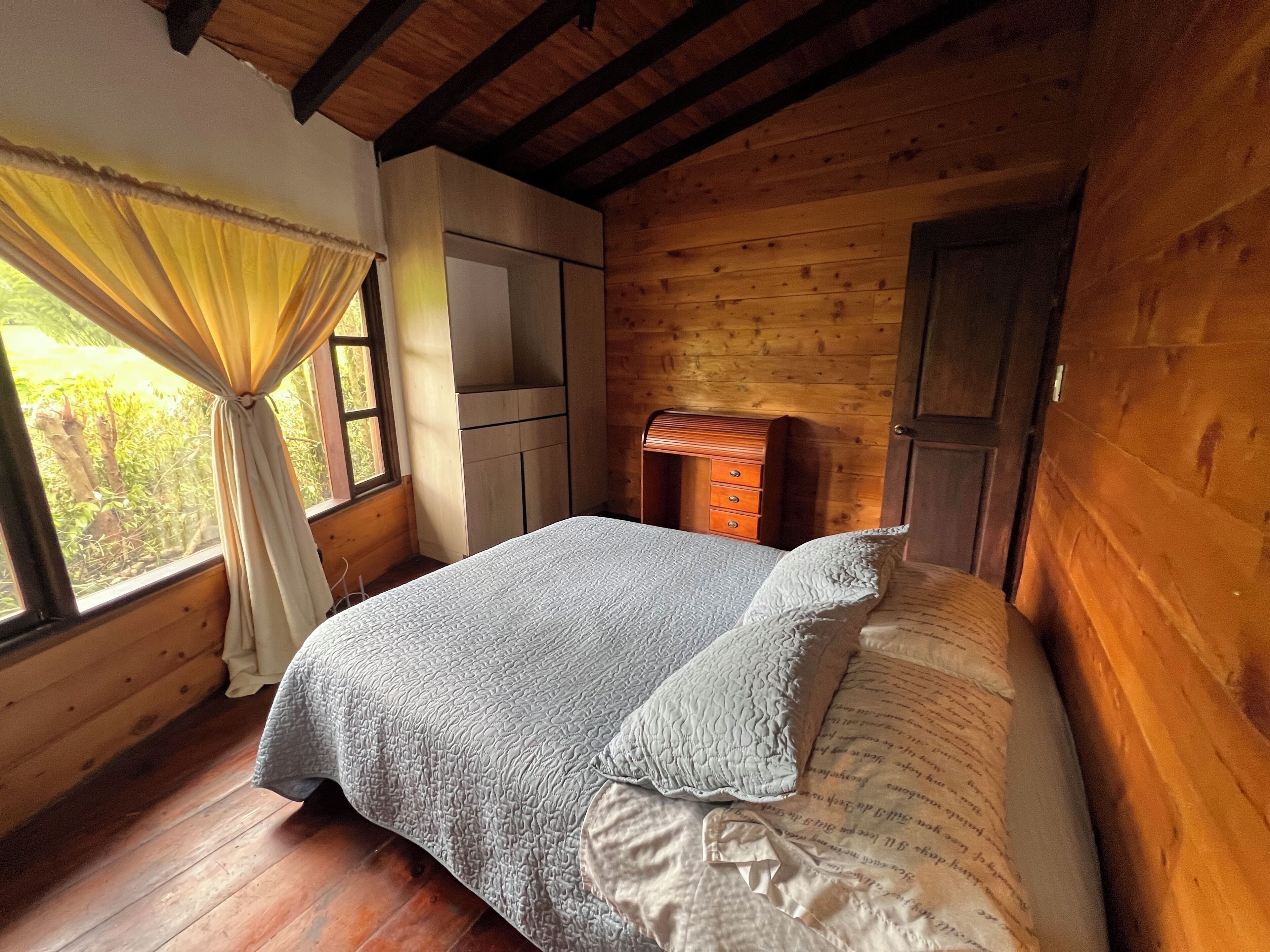A wooden room with a bed, a dresser, and a window with curtains.