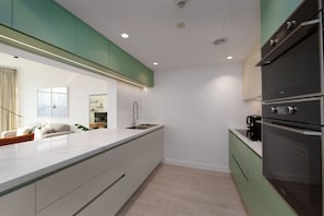 Una cocina moderna con una isla grande, armarios verdes y electrodomésticos integrados.
