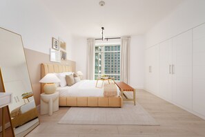 Ein modernes Schlafzimmer mit einem großen Bett, Nachttischen, einem Spiegel und Blick auf eine Stadtlandschaft durch das Fenster.