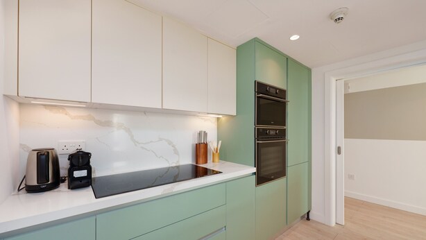 A modern kitchen with a white countertop, green cabinets, and a built-in oven.