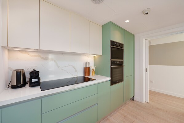 A modern kitchen with a white countertop, green cabinets, and a built-in oven.