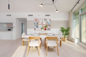 Un comedor moderno con una mesa blanca para cuatro, sillas de madera y un amplio ventanal con luz natural.