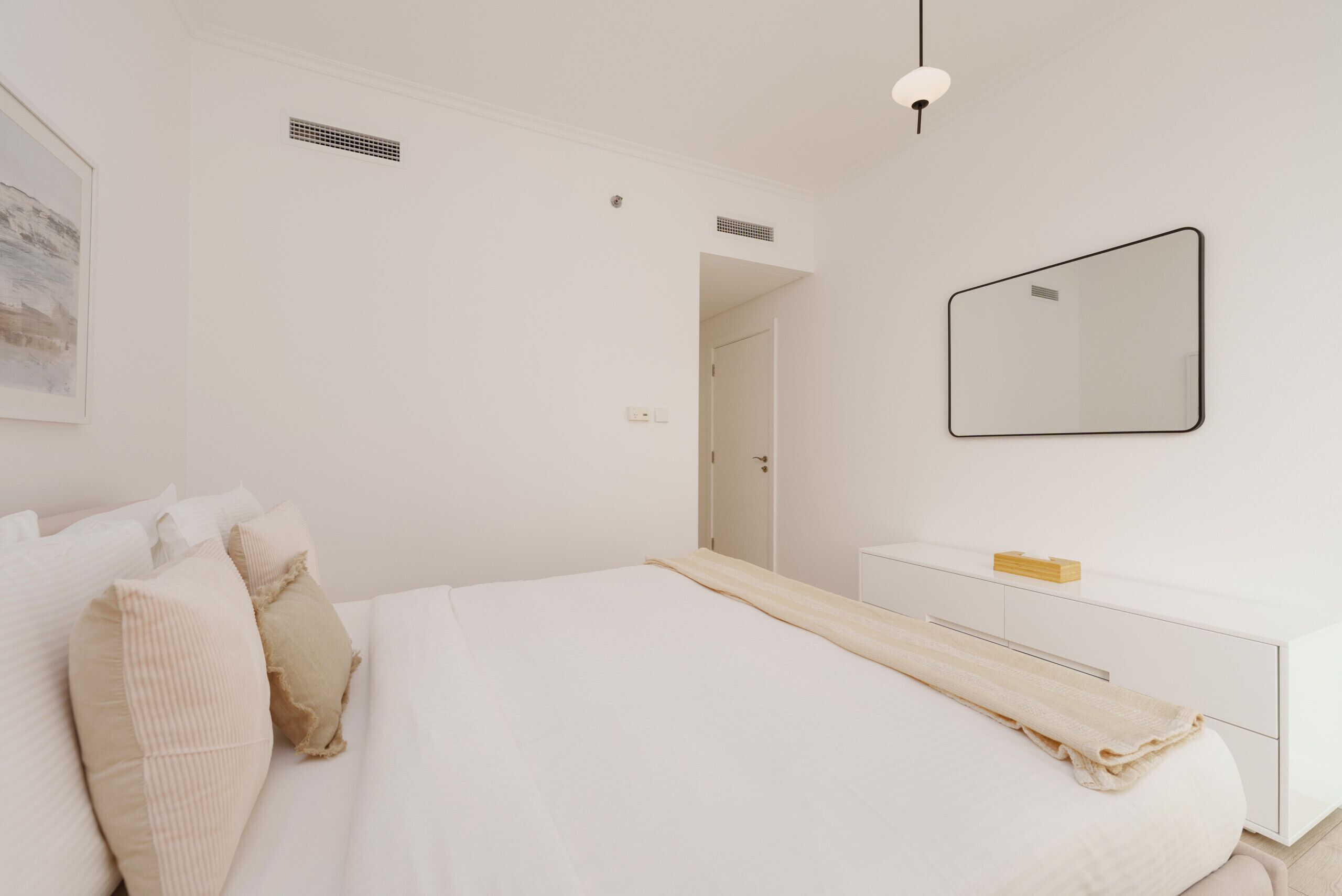 A minimalist bedroom with a bed, bedside table, and a large mirror.