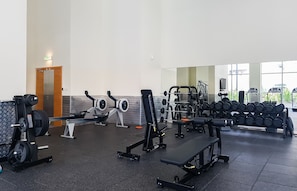 Un gimnasio con equipamiento de levantamiento de pesas, bancos y mancuernas.