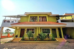 A two-story building with a green facade, a red-tiled roof, and a covered front porch with steps leading to the entrance. - Ocean Dream Luxury Villa (Arpora)