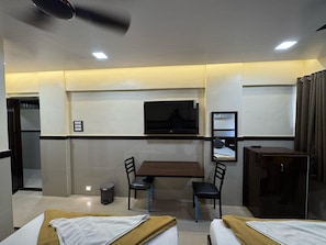 A hotel room with two beds, a desk, chairs, a television, and a wardrobe. - Sai Residency & Dormitory (Thane)