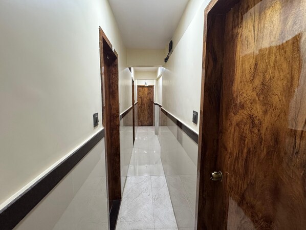 A hallway with wooden doors and white walls. - Sai Residency & Dormitory (Thane)