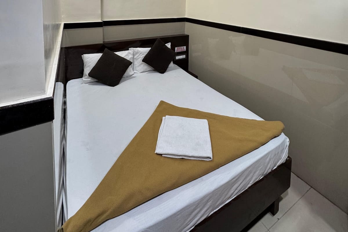 A neatly made bed with a brown blanket and a folded white towel, a black headboard, and a white wall with a black border.