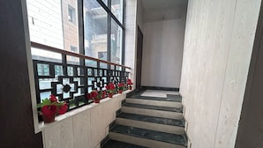 A staircase with black steps and white walls, leading to a landing with a black metal railing and red flowers. - Hotel B K House (Noida)