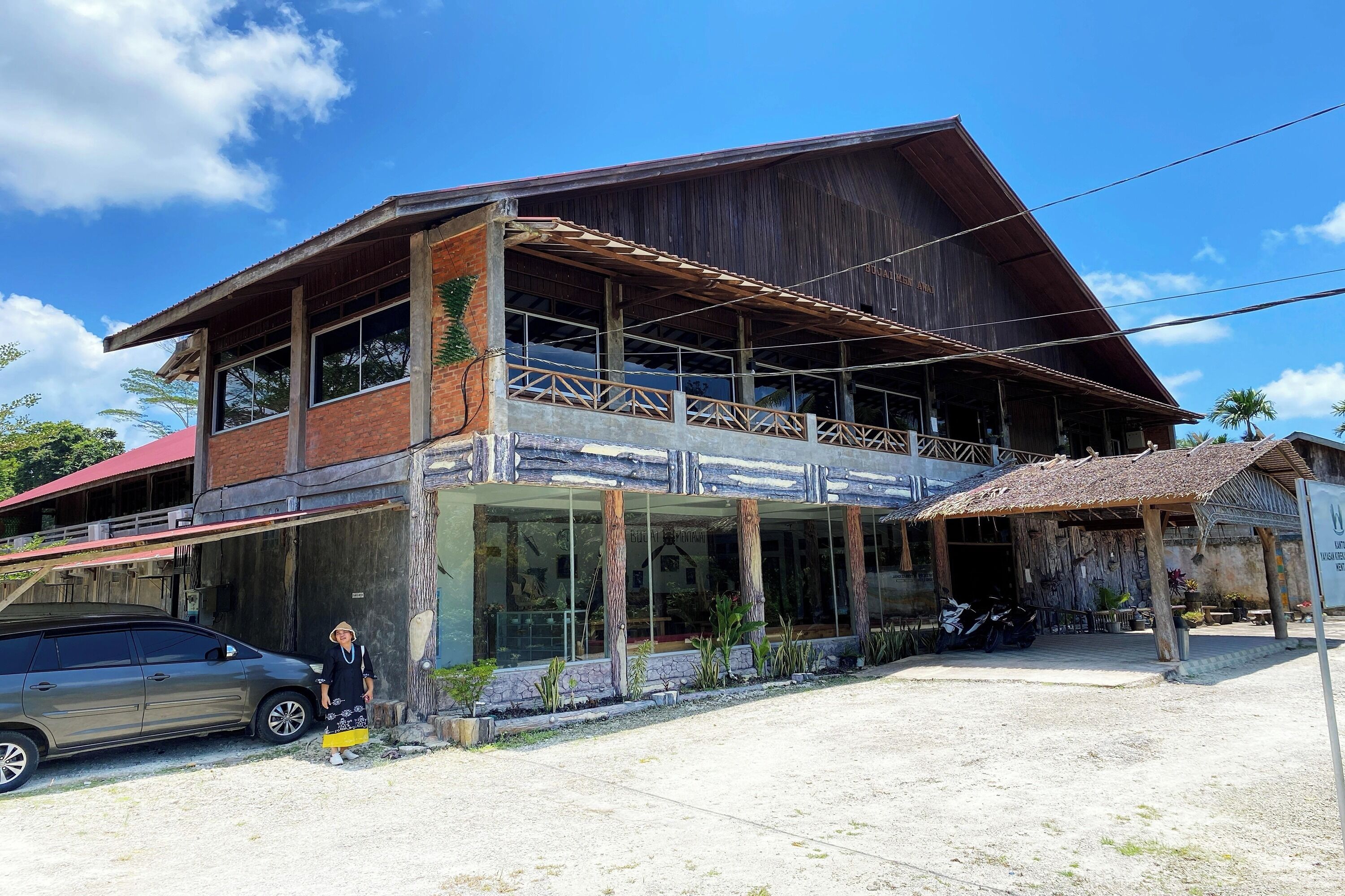 A two-story building with a balcony, a car parked in front, and a person standing near the entrance.