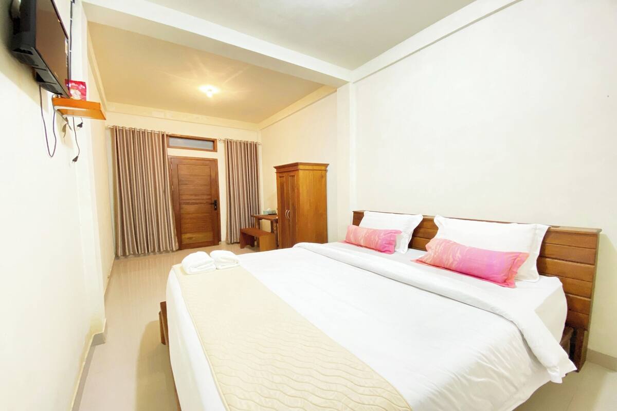 Una habitación de hotel con una cama grande, cabecero de madera y un televisor fijado a la pared.