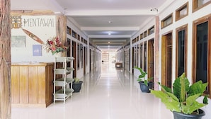 A hotel corridor with a reception desk labeled "MENTAWAI," potted plants, and a clean, tiled floor.