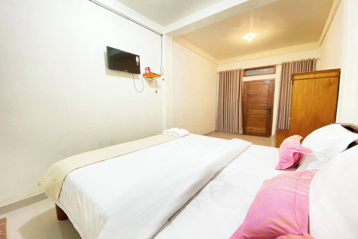 Habitación de hotel con cama, televisor montado en la pared, puerta de madera y ventana con cortinas.