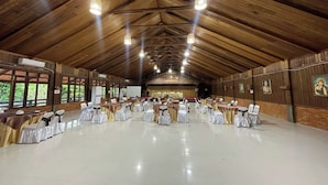 A large hall with wooden ceiling beams, rows of tables with chairs, and a stage at the front.