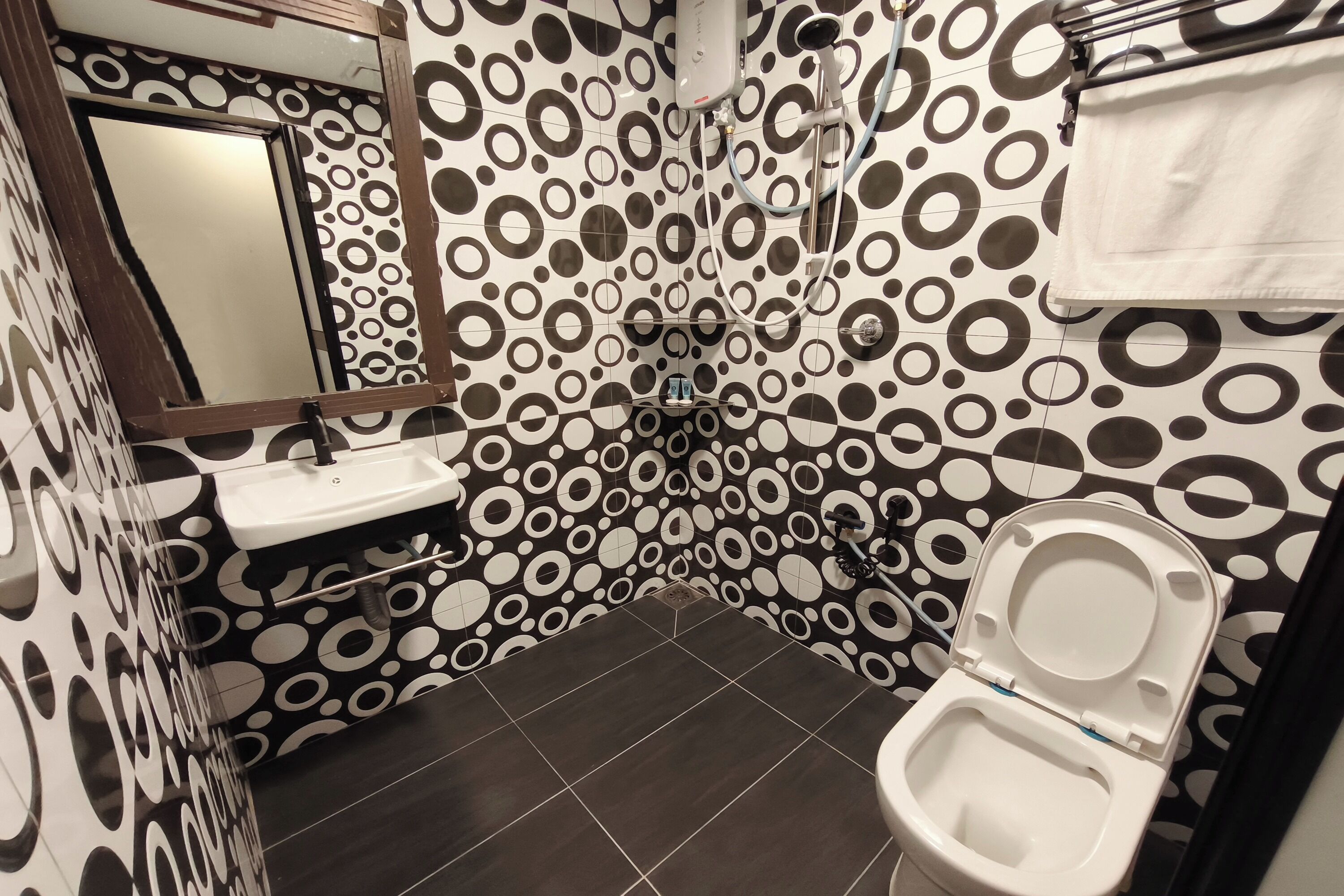 A bathroom with a toilet, sink, and mirror. The walls have a black and white circular pattern.