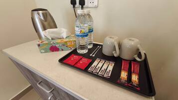 Balcão de quarto de hotel com cafeteira, duas garrafas de água, caixa de lenços, bandeja com sachês de açúcar e duas canecas.