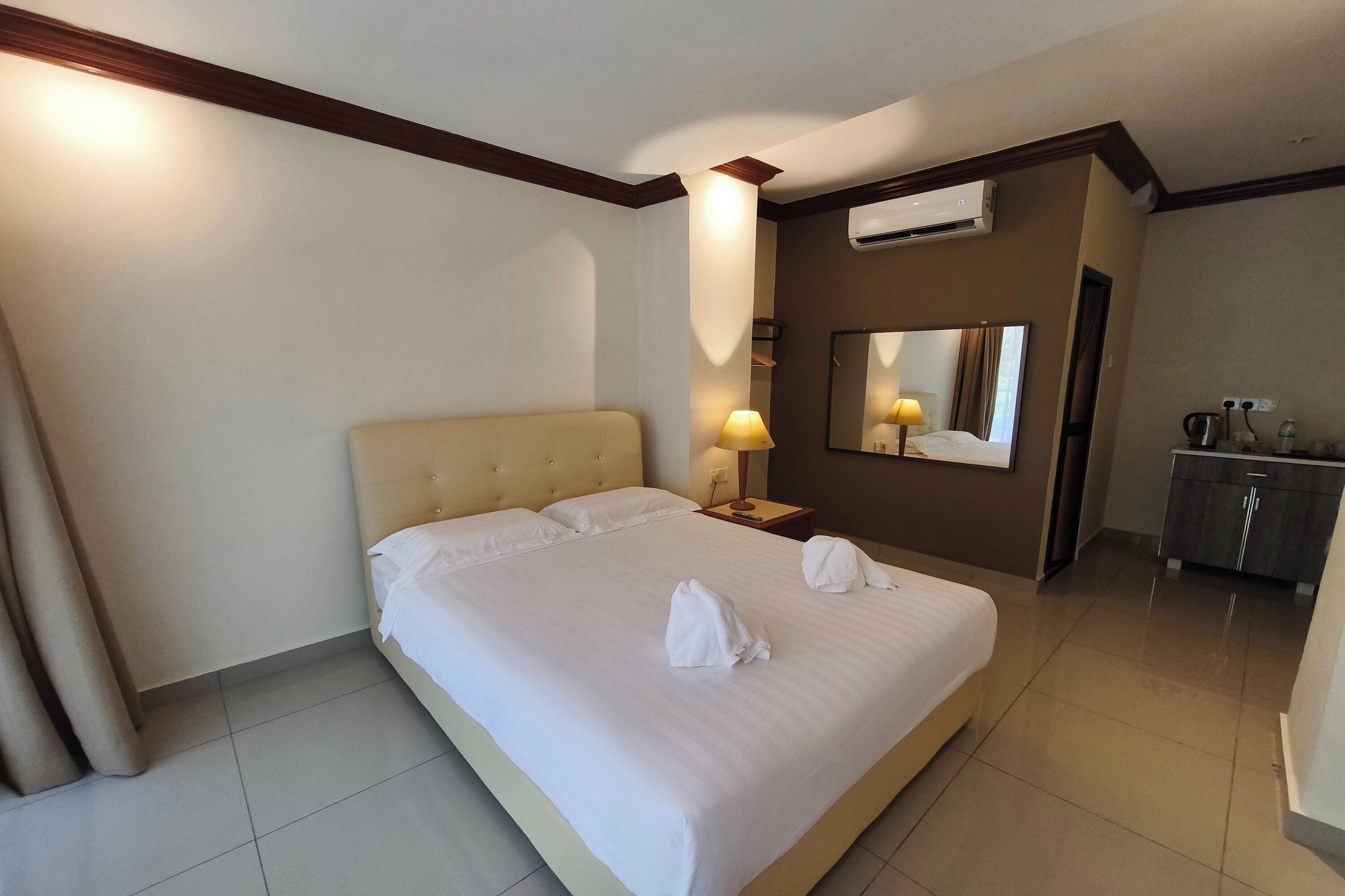 A hotel room with a large bed, a bedside table with a lamp, a mirror, and a wardrobe.