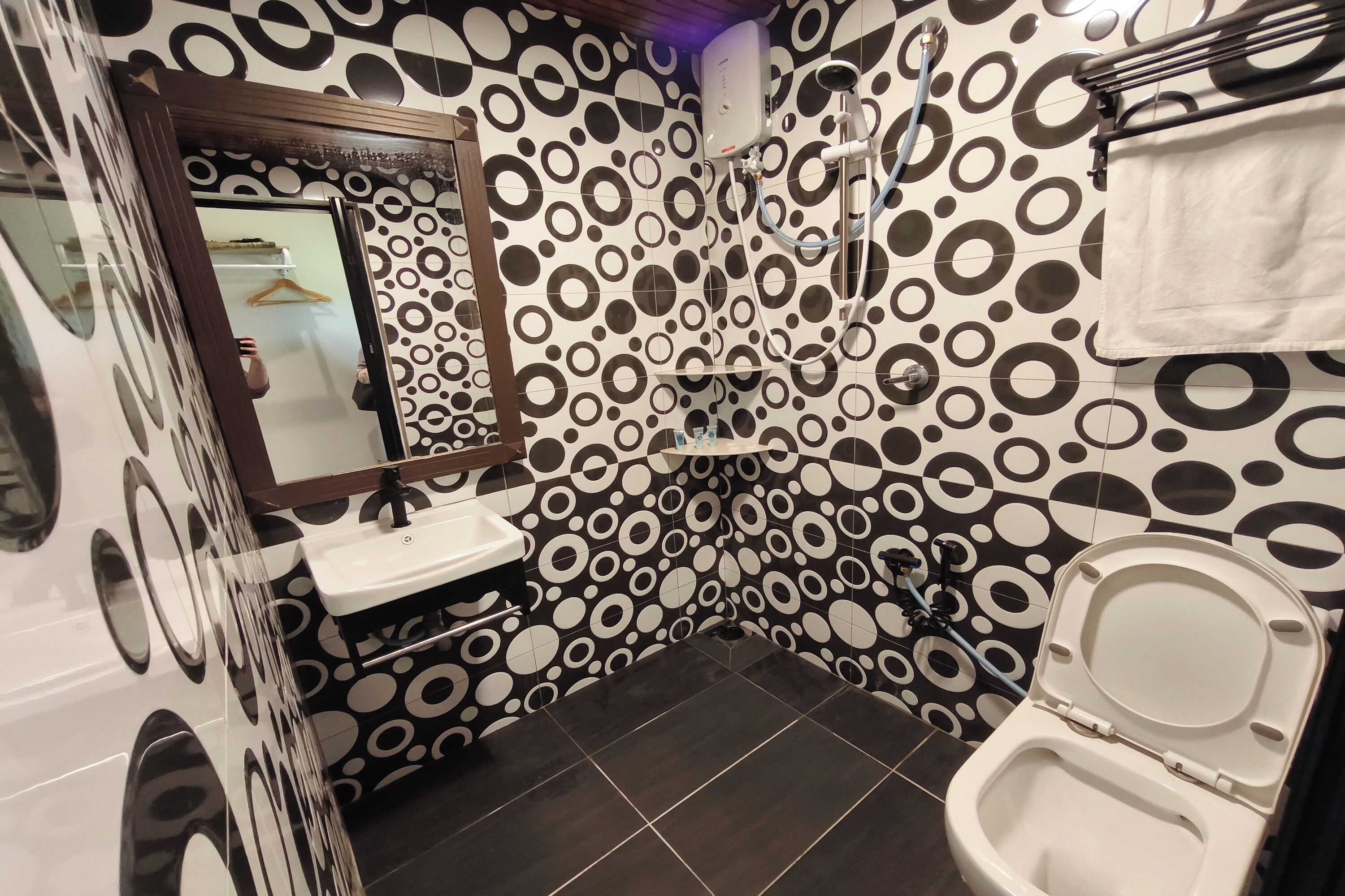 A bathroom with a toilet, sink, and shower. The walls have a black and white circular pattern.