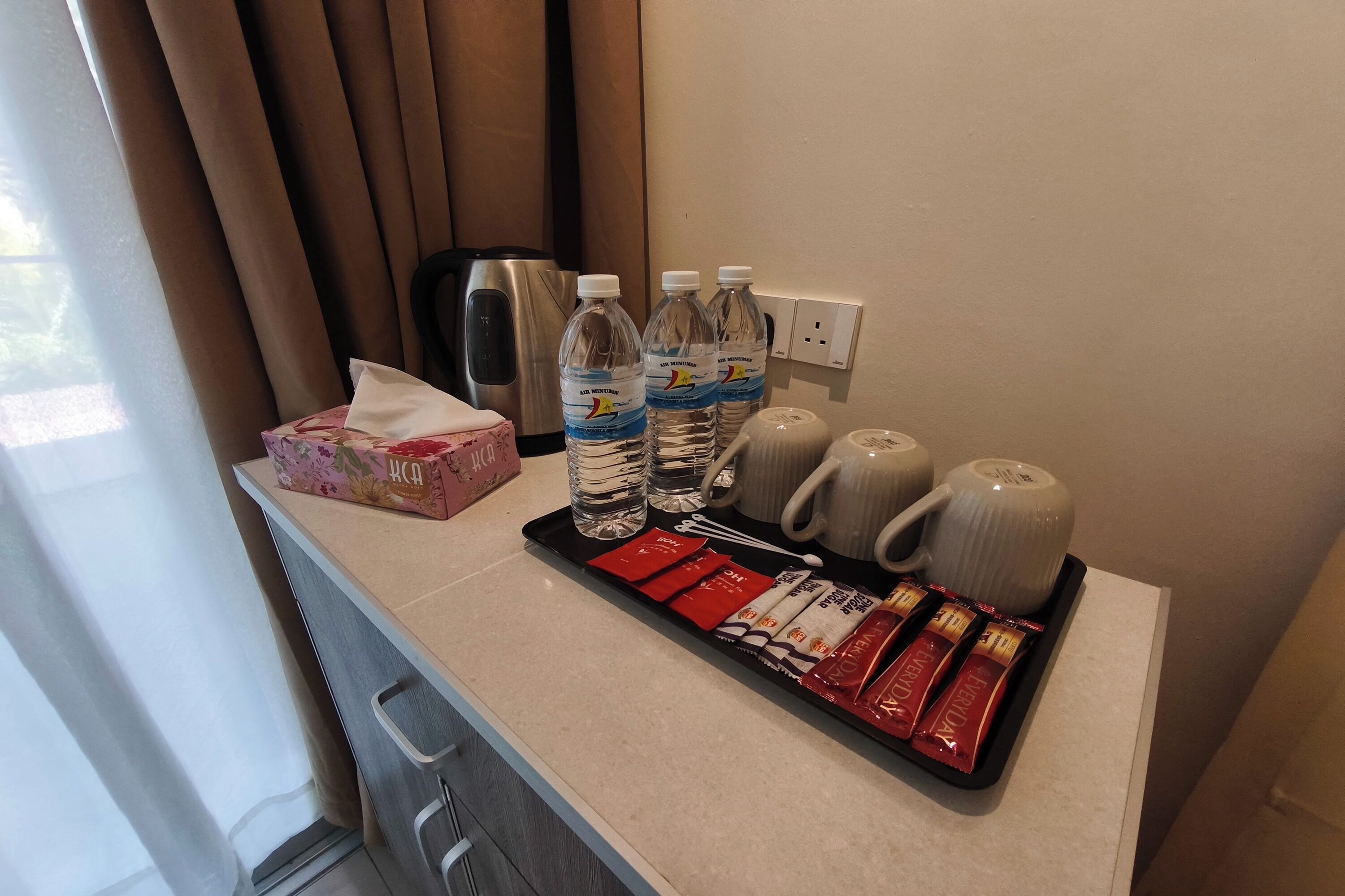 Un mini-bar d’hôtel contenant des bouteilles d’eau, des sachets de café et une boîte de mouchoirs.