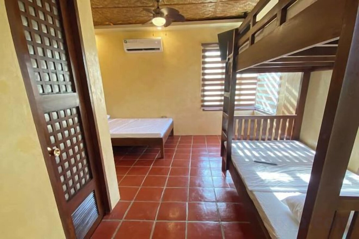 A room with bunk beds, a window with blinds, a door with a decorative panel, and an air conditioning unit.