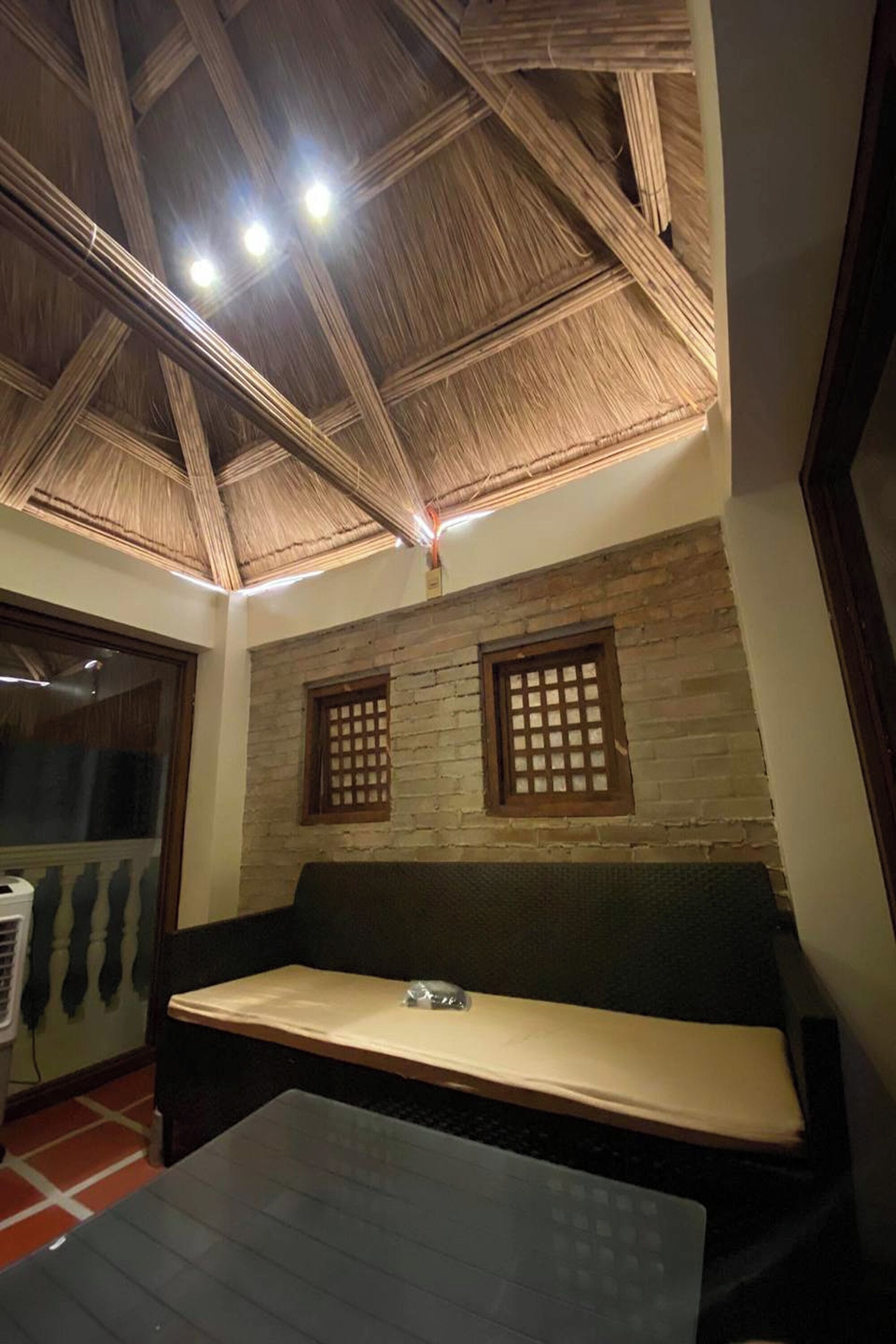 A room with a thatched ceiling, a stone wall, a wooden bench, and a small table.