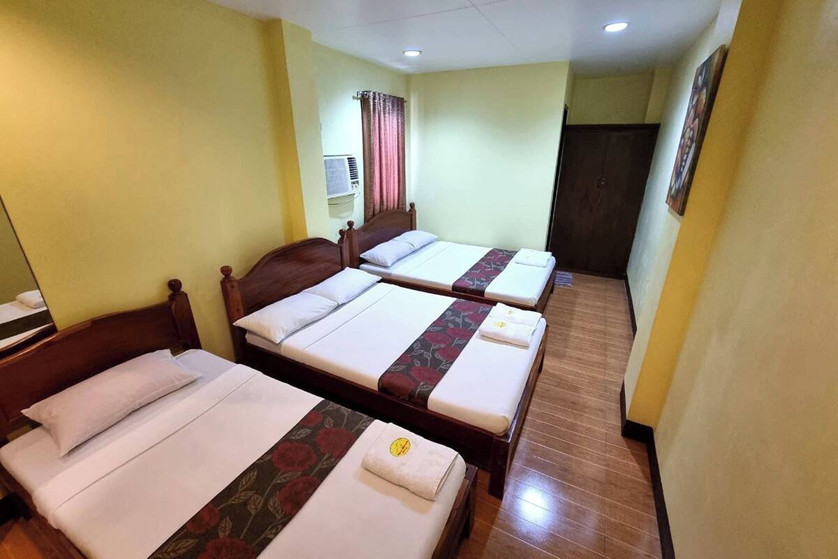 Une chambre d’hôtel avec deux lits simples, une tête de lit en bois, une petite table de chevet, un appareil de climatisation et une porte.