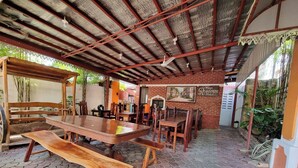 Un espace de restauration extérieur abrité, avec des tables et des chaises en bois, un mur en briques et une enseigne indiquant « Hôtel Résidence ».