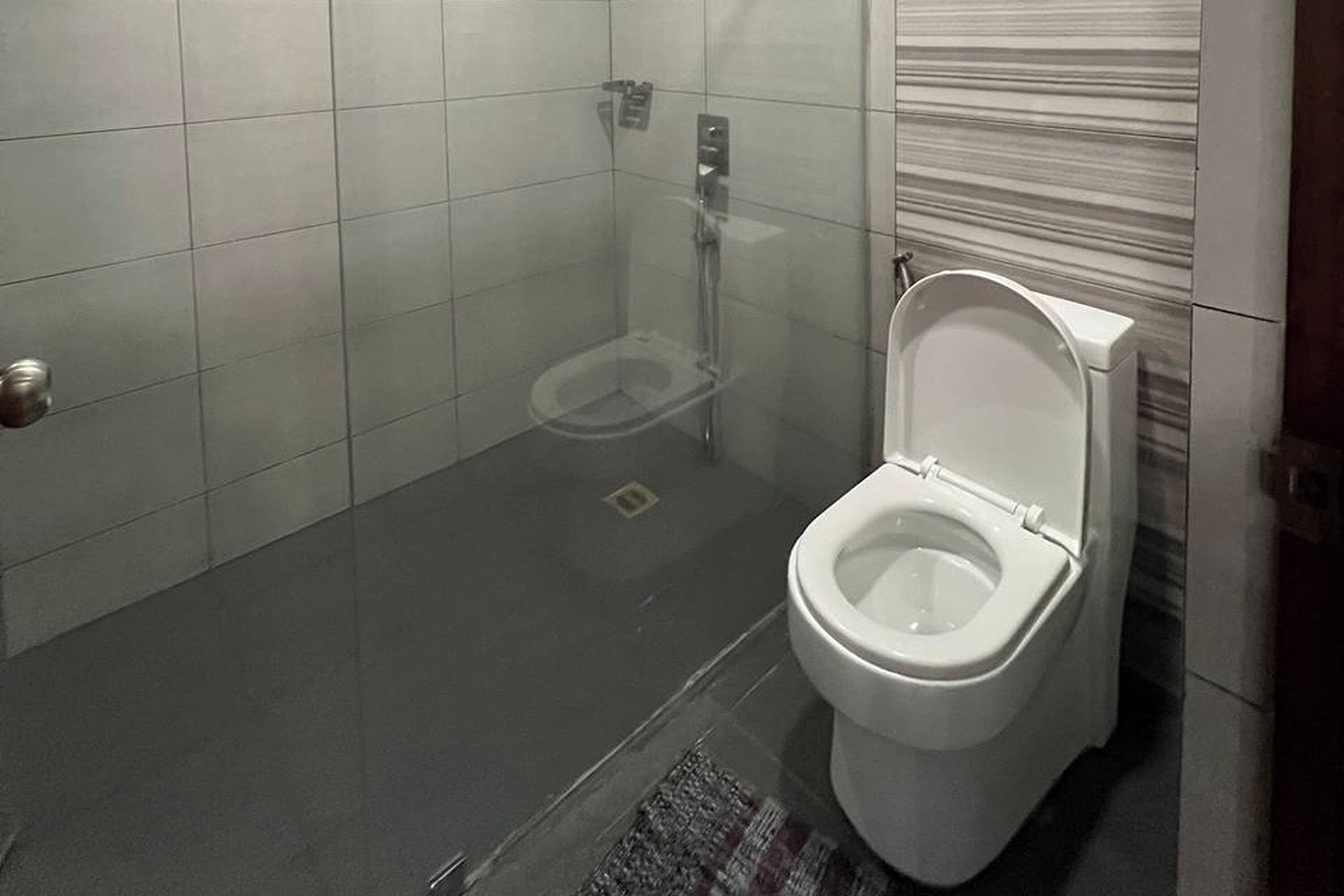 A bathroom with a toilet, a shower, and a tiled floor.