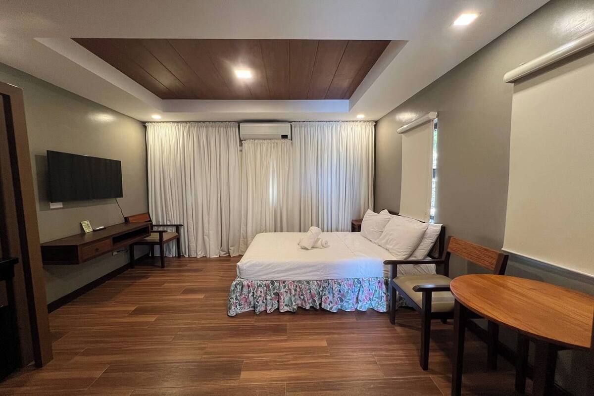 A hotel room with a bed, a desk, a chair, a TV, and a window with curtains.