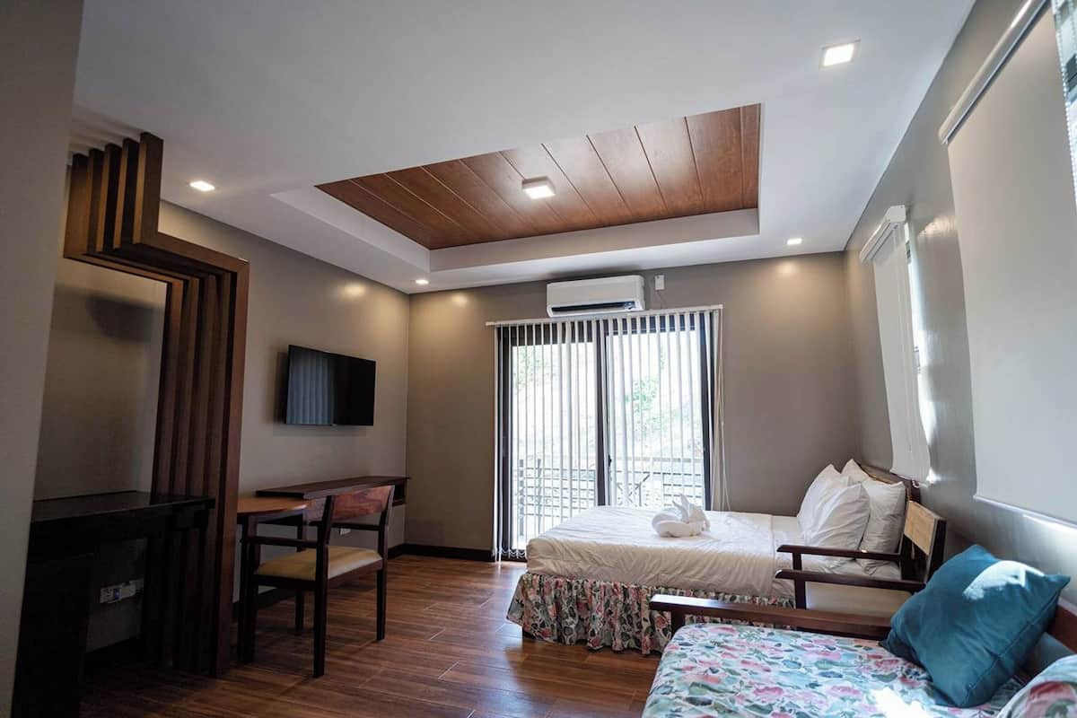 A bedroom with a bed, a desk, and a chair. There is a window with blinds, a ceiling fan, and an air conditioning unit.