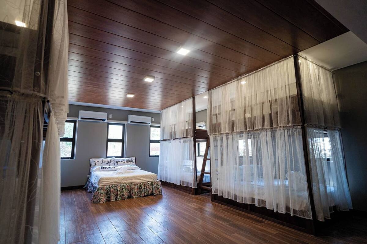 A bedroom with a wooden floor, a bed with a floral bedspread, and sheer curtains.