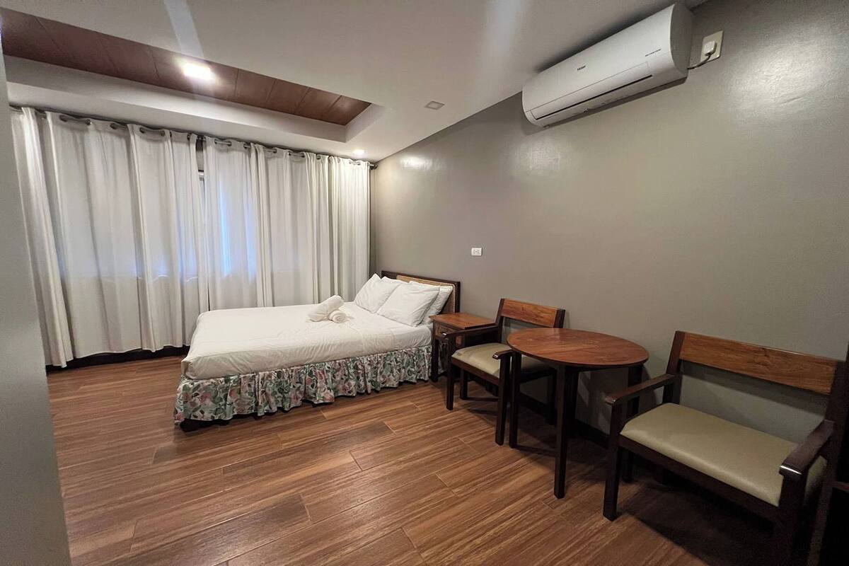 A bedroom with a bed, a small table, two chairs, and an air conditioning unit.