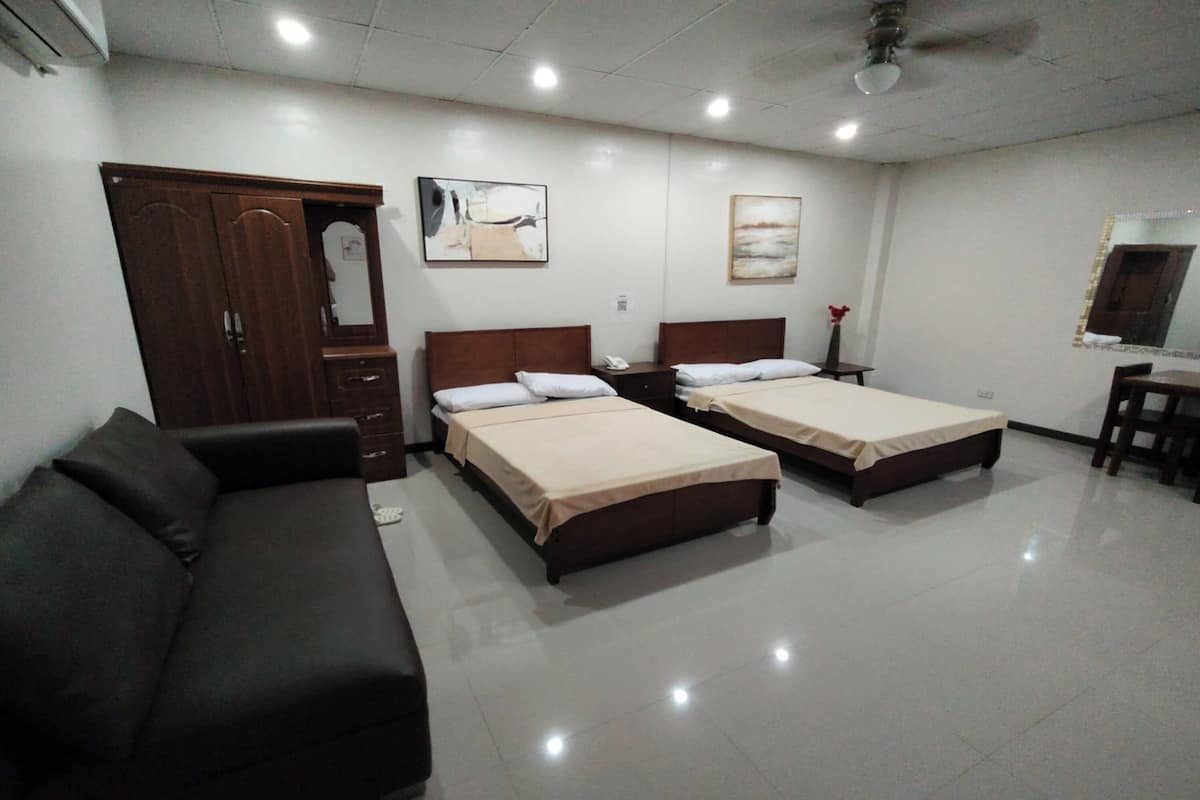 A hotel room with two single beds, a sofa, a desk, and a mirror.