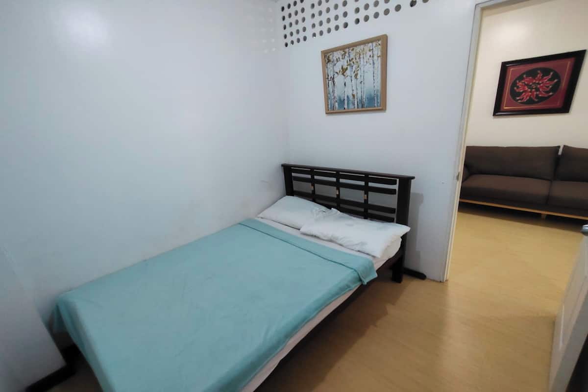 A small, single-bed room with a light blue bedspread, a wooden headboard, and two framed pictures on the wall.