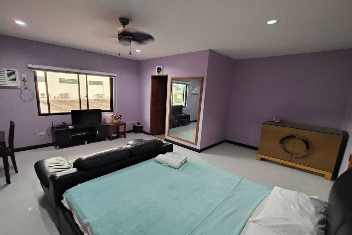 A bedroom with a bed, a TV, a dresser, a mirror, and a window.
