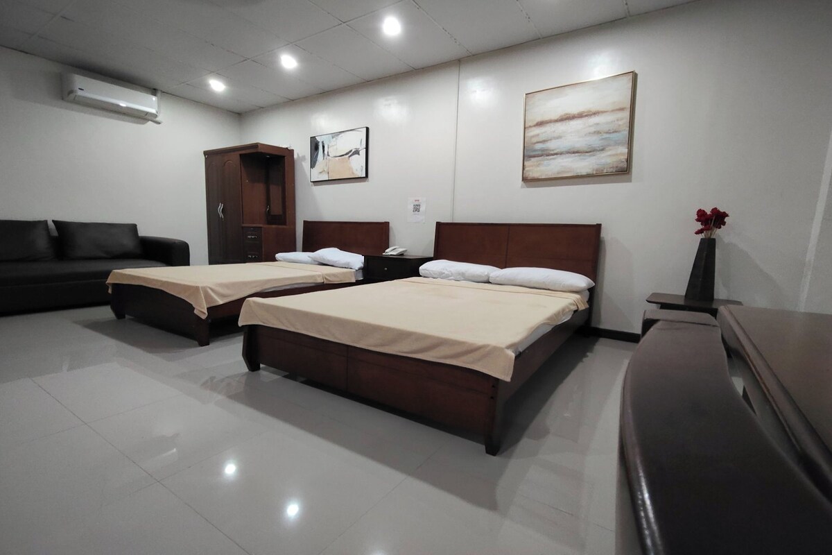 A hotel room with two beds, a sofa, a desk, and a cabinet.