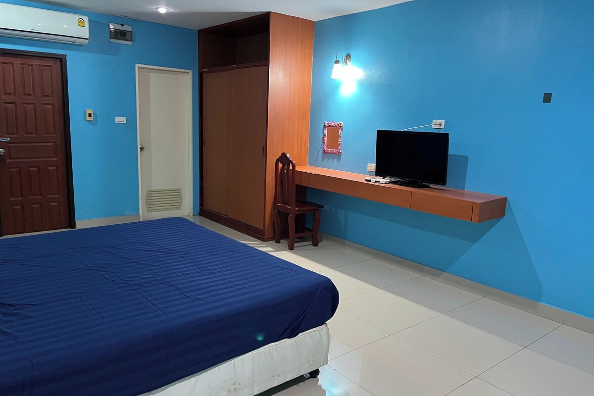 A bedroom with a bed, a desk with a TV, a wardrobe, and a door.