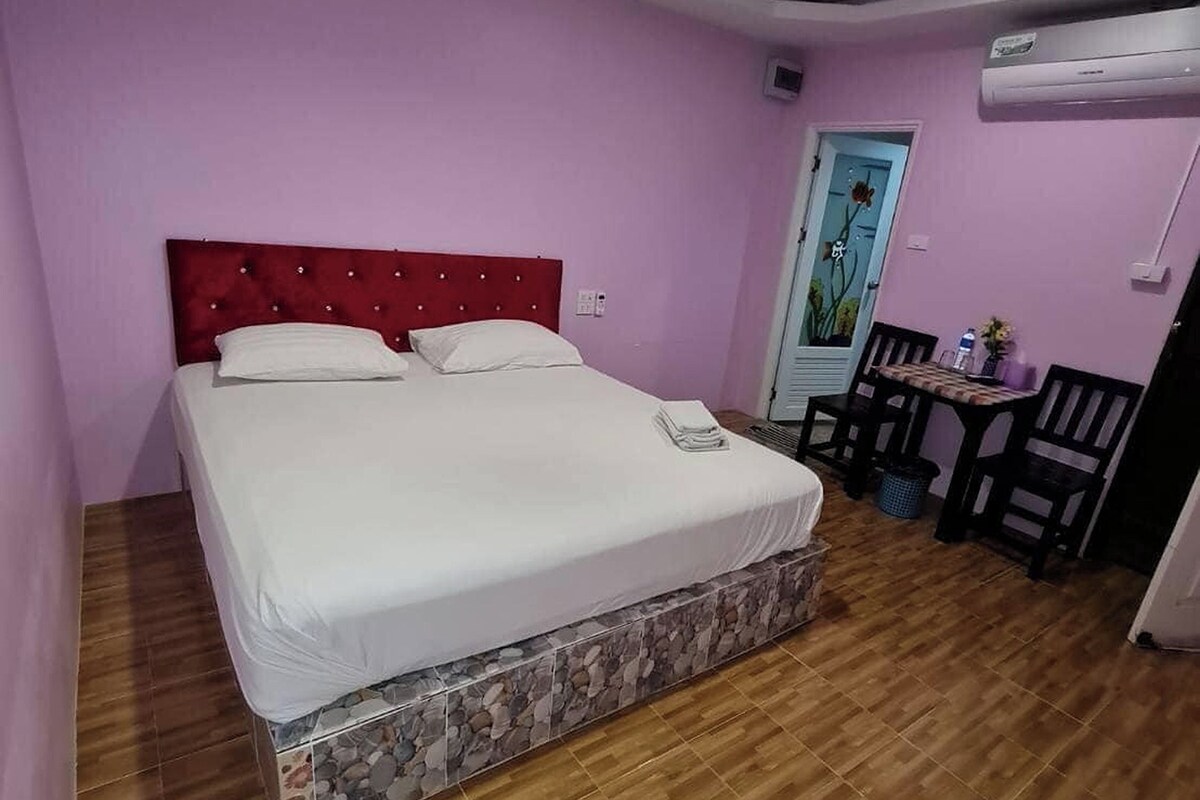 A hotel room with a large bed, a small table with chairs, and an air conditioning unit on the wall.