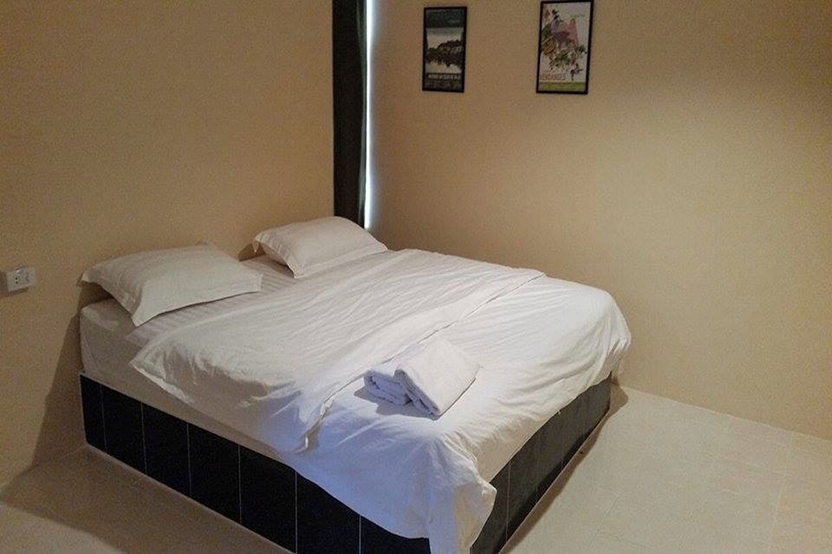 Ein ordentlich bezogenes Bett mit weißen Leinen und einem gefalteten Handtuch daneben.