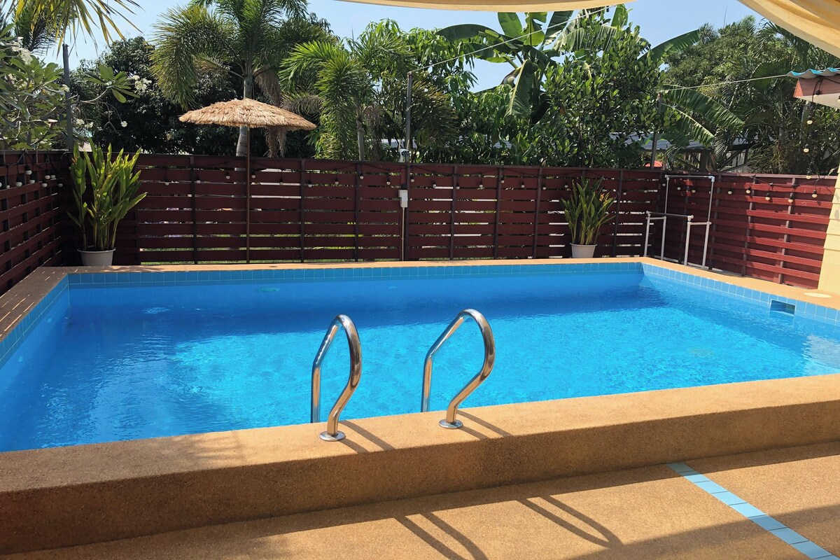 Ein Schwimmbecken mit Metallhandläufen, umgeben von einem Holenzaun und Topfpflanzen.