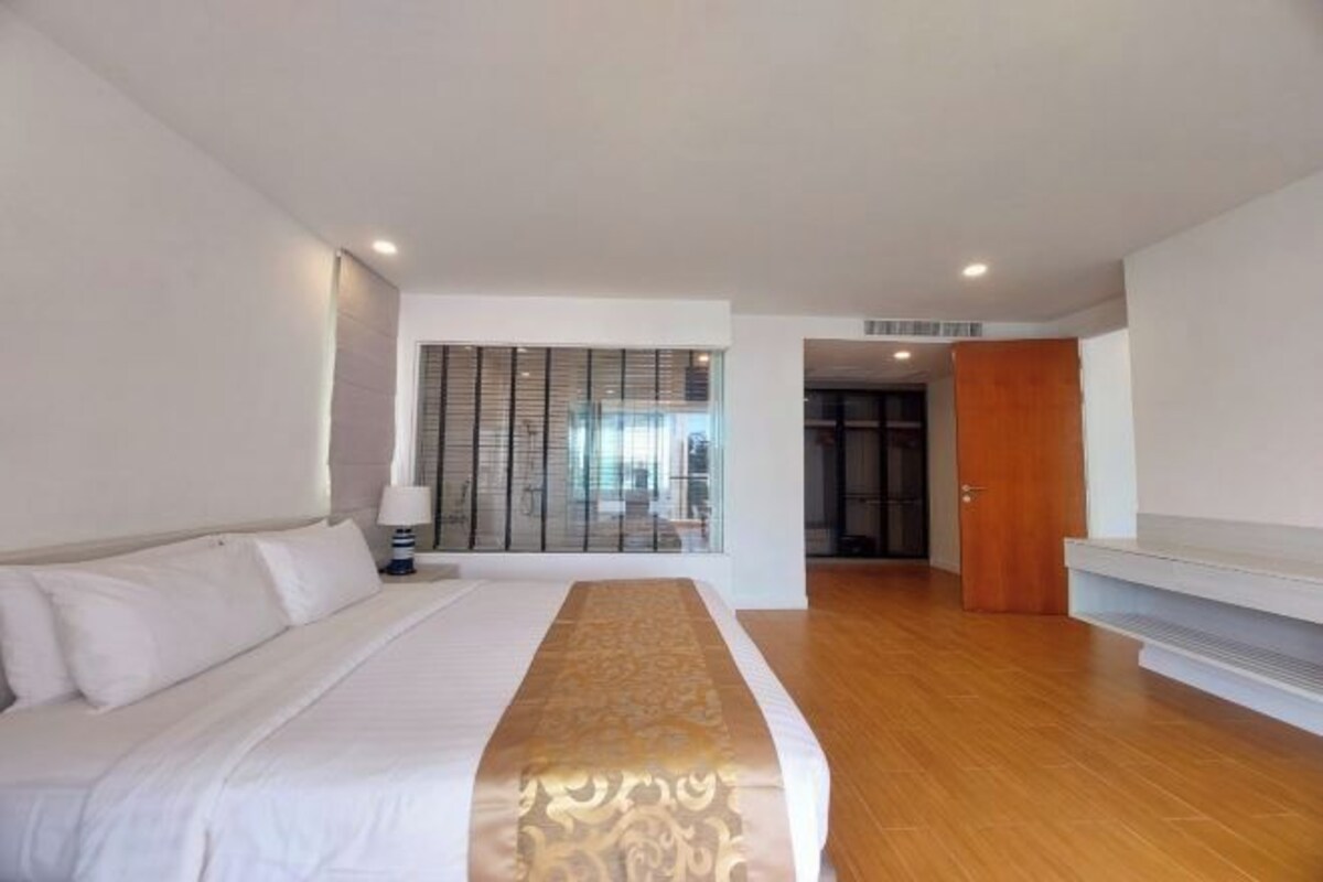 Une chambre d’hôtel moderne avec un grand lit, un plancher en bois, une vue à travers un mur de verre et une porte en bois.