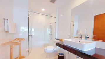 A modern bathroom with a glass shower enclosure, a white toilet, a large white sink, and a wooden towel rack.