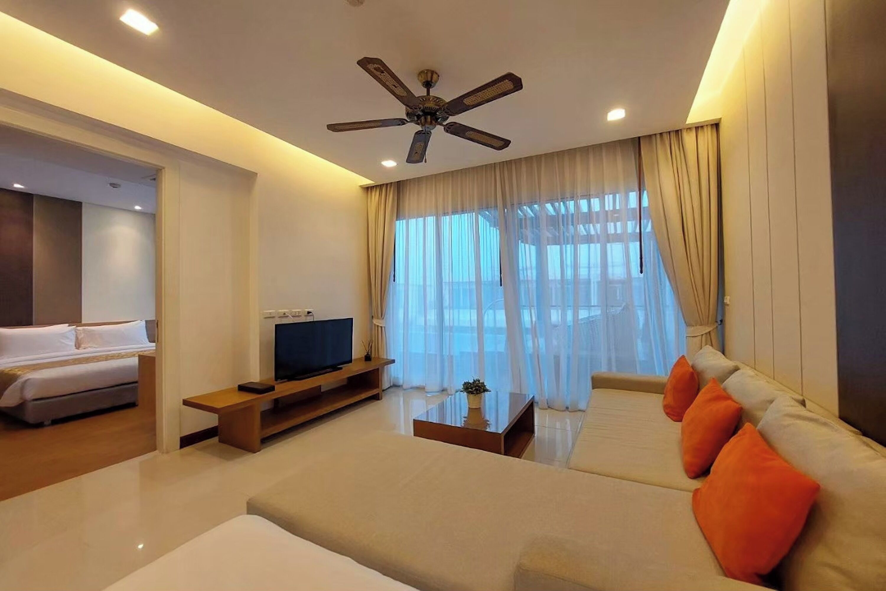 A modern hotel room with a large bed, a sofa, a TV, and a ceiling fan.