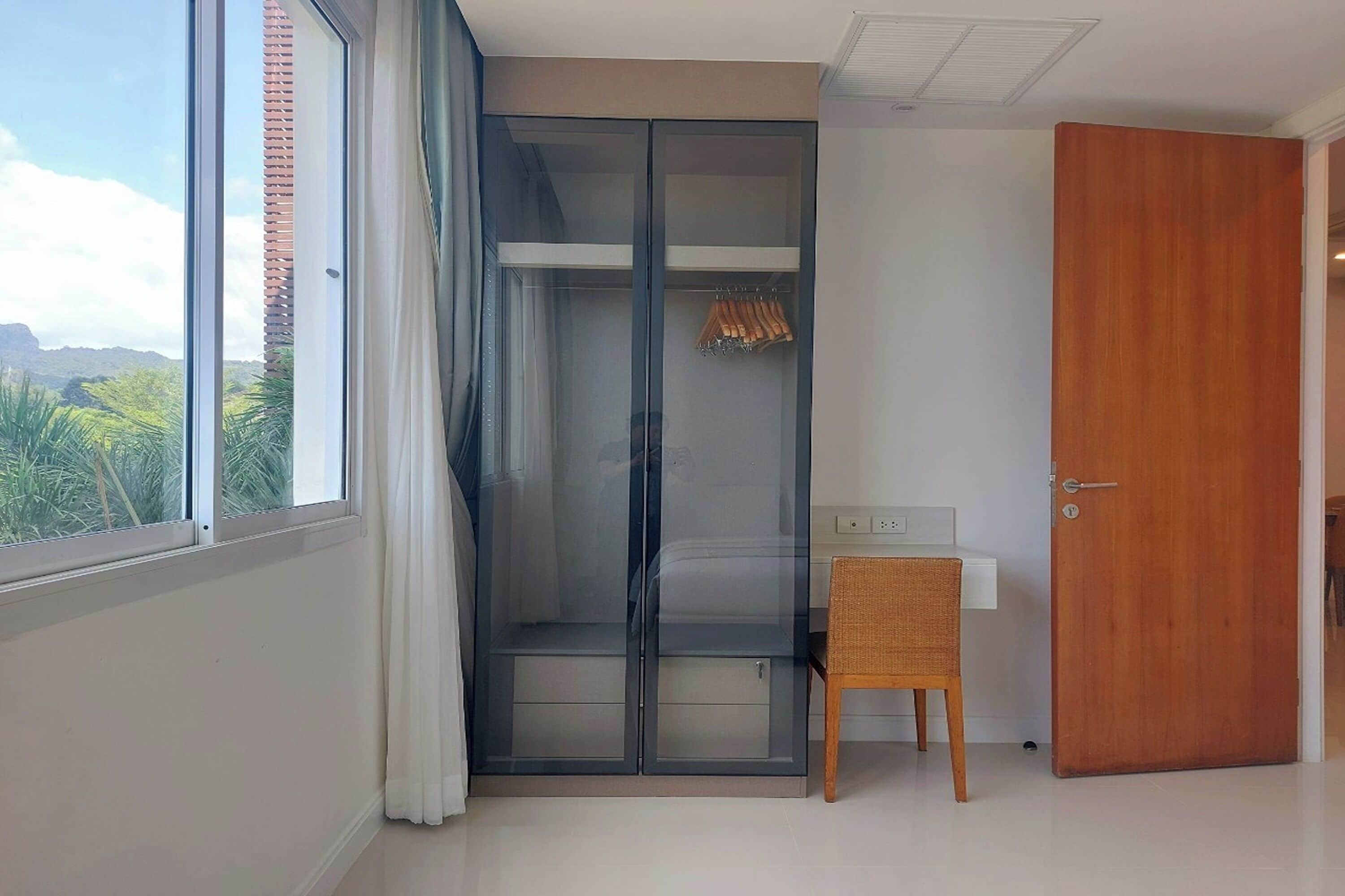 Une pièce avec un placard à portes coulissantes en verre, une petite chaise en bois et un bureau blanc.