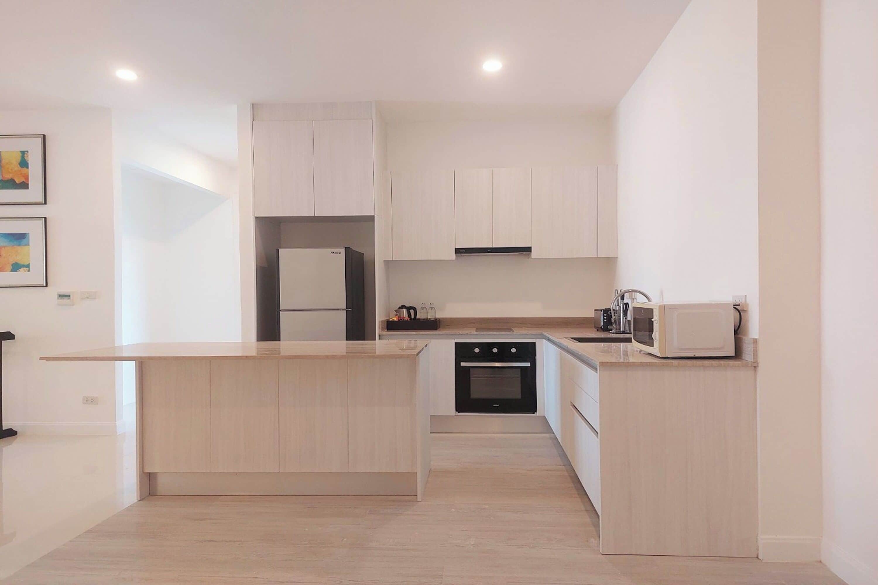 A modern kitchen with light wood cabinets, a built-in oven, a microwave, and a stainless steel refrigerator.